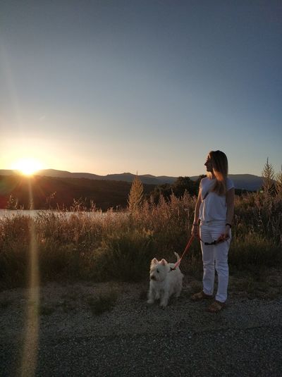 Woman with dog standing on field during sunrise