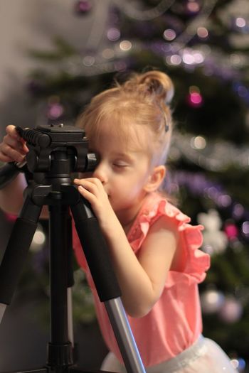 Girl holding tripod while standing against christmas tree