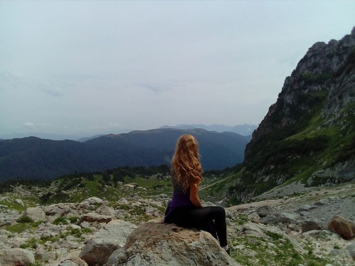 Side view of woman sitting on mountain against sky