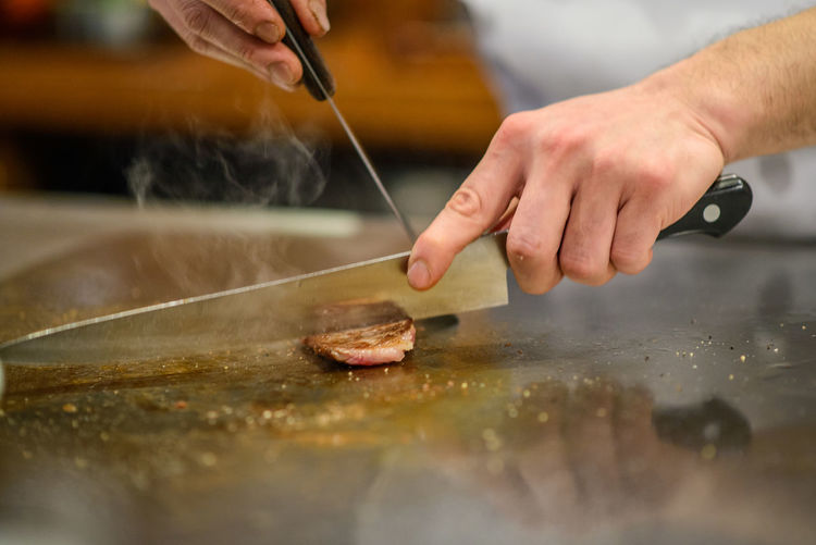 Close-up of chef's hand cutting and preparing steak