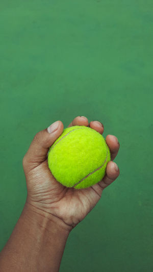 Cropped image of person holding ball against green background