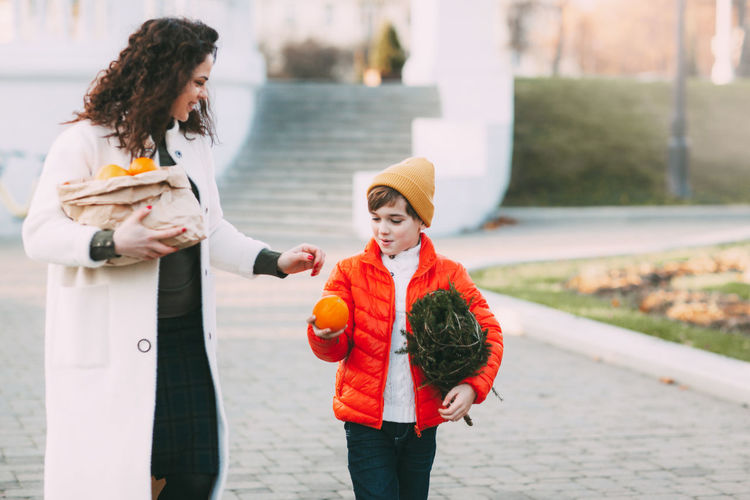 A beautiful mother with her son in a bright orange jacket and a fashionable yellow hat are walking 