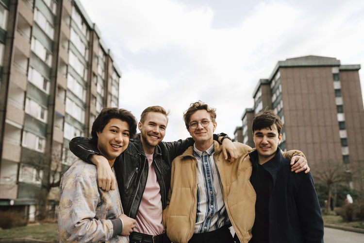 Portrait of smiling male friends with arms around in city
