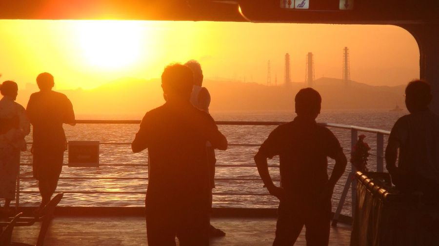 Silhouette people standing on railing at sea during sunset