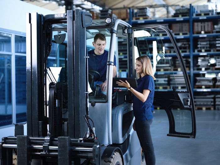 Engineer showing tablet pc with worker in forklift at factory