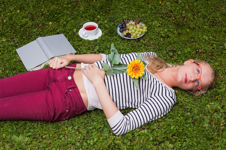 High angle view of young woman holding flower while lying on grassy field