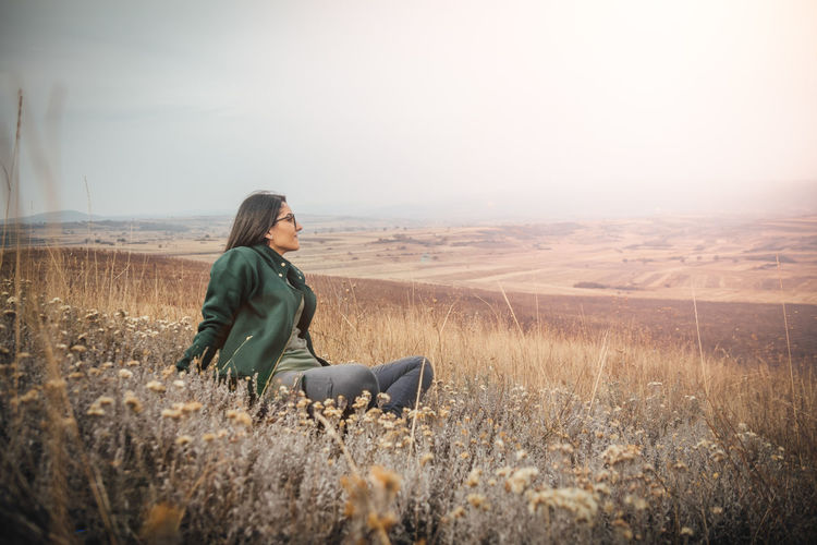 Young woman sitting on field against sky