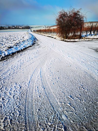 Tire tracks on snow covered road against sky