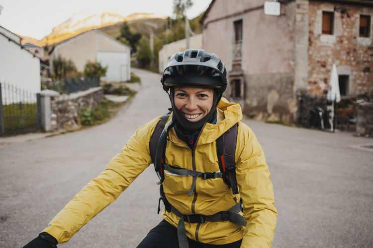 Smiling mid adult woman in warm clothing riding mountain bike on road while traveling to somiedo natural park, spain