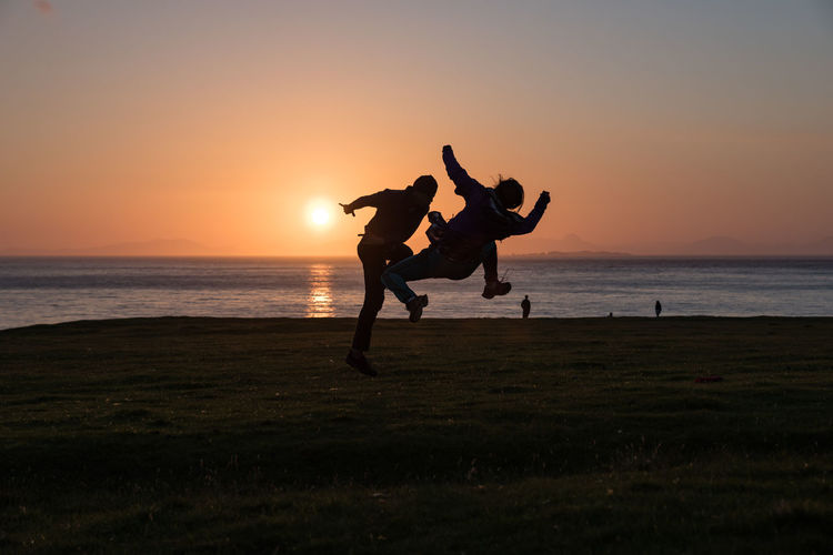Silhouette people on beach against sky during sunset