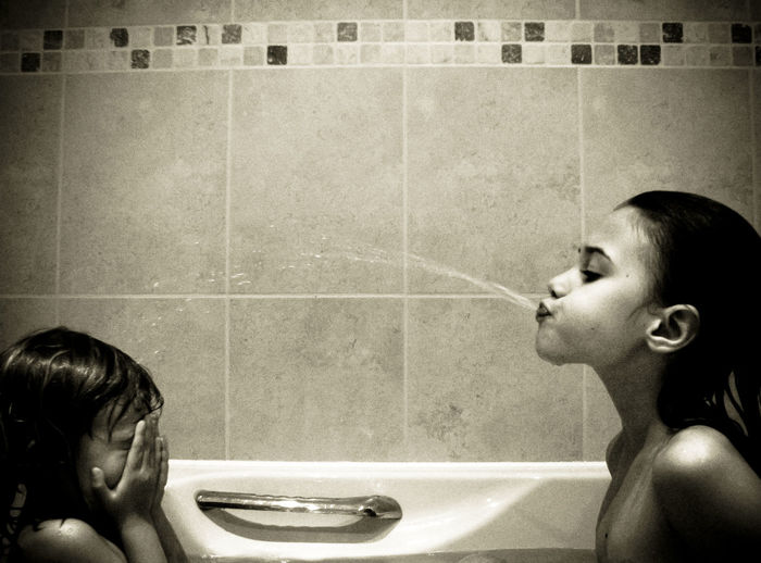 Girl spitting water on sister in bathtub