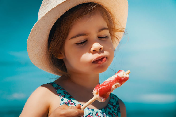 Cute girl looking away while eating ice cream at beach