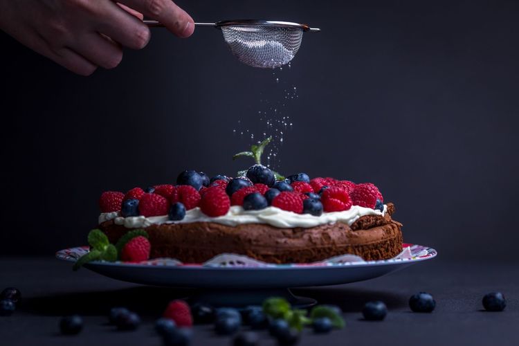 Cropped image of hand pouring powdered sugar into cake