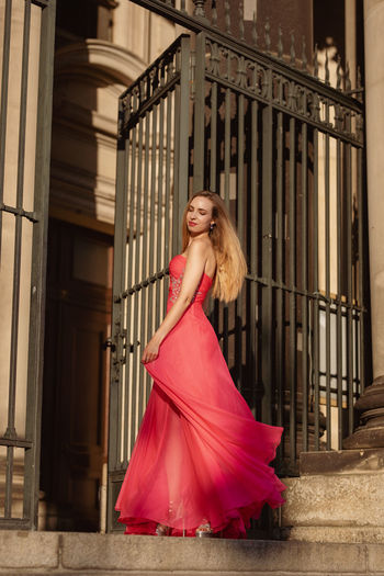 Low angle side view of beautiful woman in pink evening gown standing at doorway