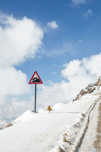Road sign on snowcapped mountain against sky