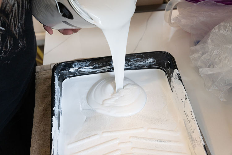 White paint is poured into a paint tray from a paint bucket