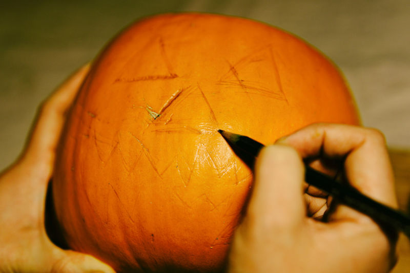 Cropped hand of person drawing on pumpkin during halloween