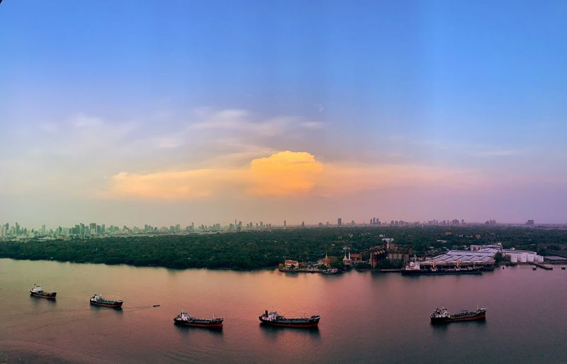 Sunset over chao phraya river with boats and bangkok cityscape in background