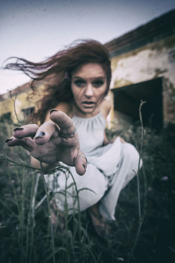 Portrait of woman looking at the camera sitting in a field while the wind moves her red hair