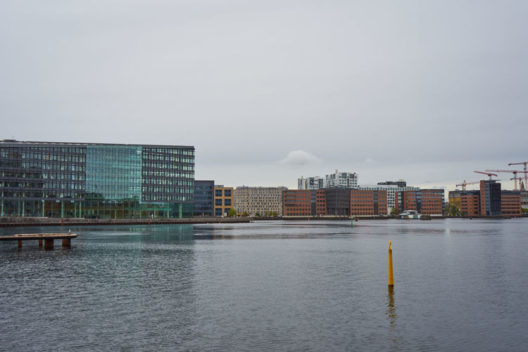 Modern buildings by river against sky in city