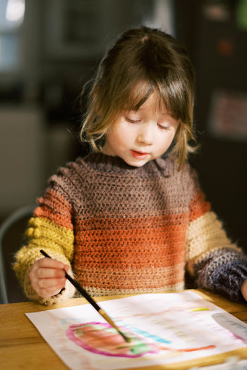 Little preschool girl painting with watercolors at the kitchen table