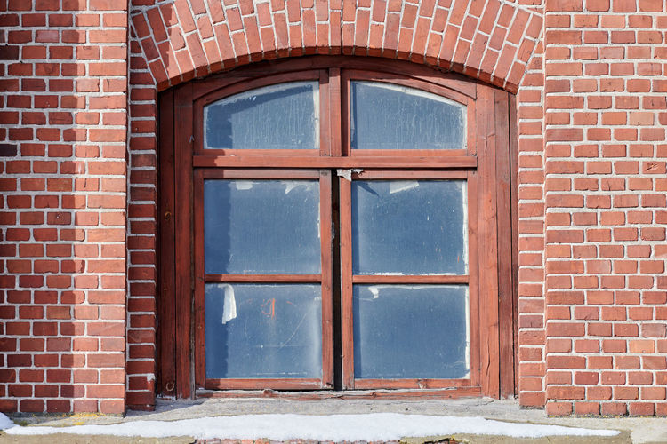 One arched glass window on old red brick wall. window in brown wooden frame on red brick wall