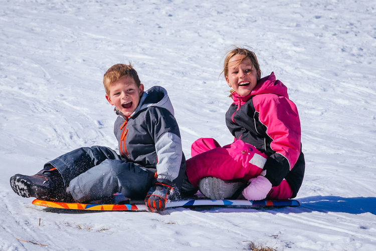 Cheerful siblings sitting on snow covered land