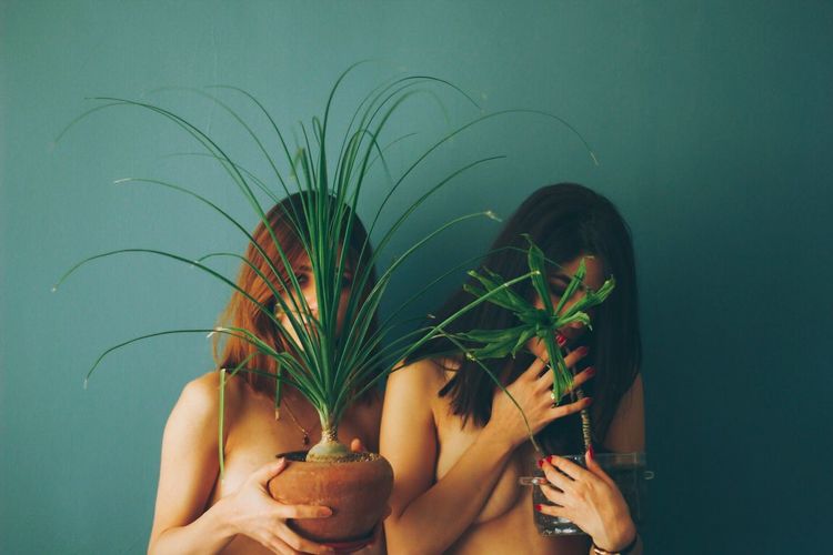 Close-up of lesbian couple holding potted plants against wall