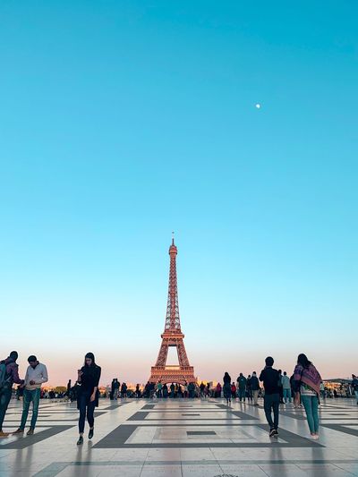 Group of people on footpath against eiffel tower at sunset