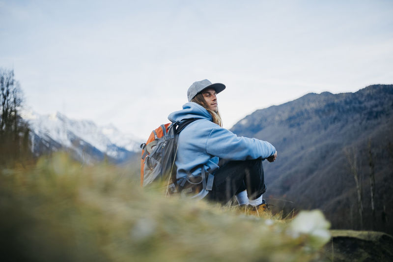 Man with backpack sitting with eyes closed on mountain