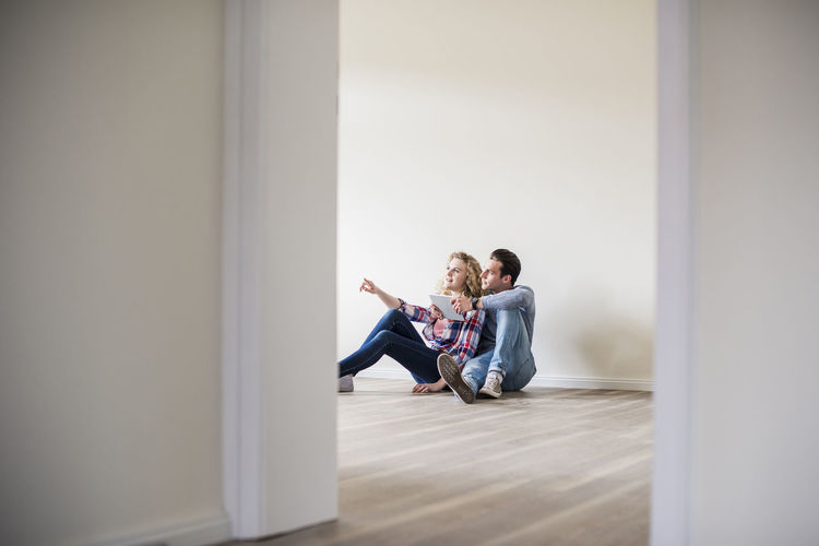 Young couple in new home sitting on floor with tablet