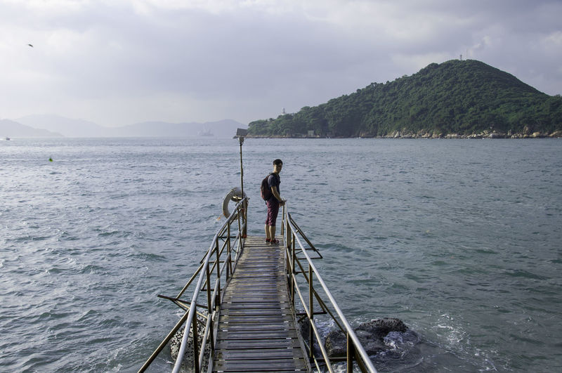 Young man standing on wooden jetty over sea against sky