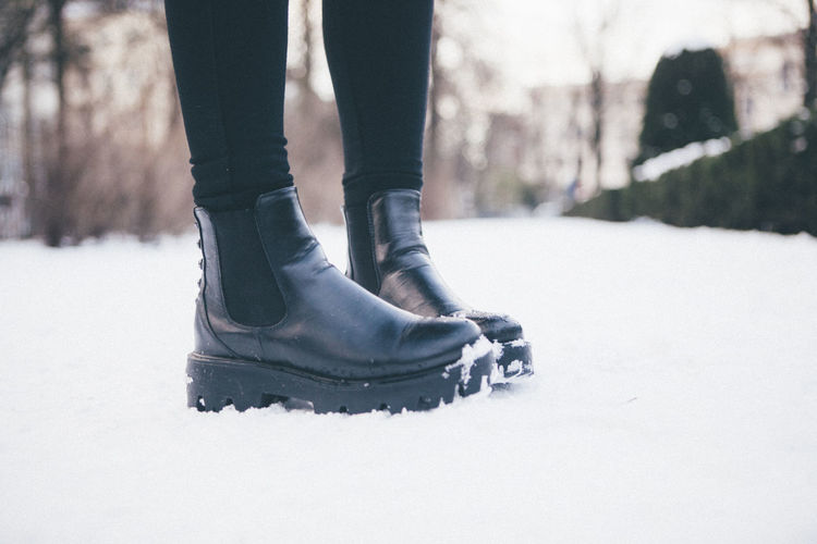 Low section of woman wearing leather boots while standing on snowy field