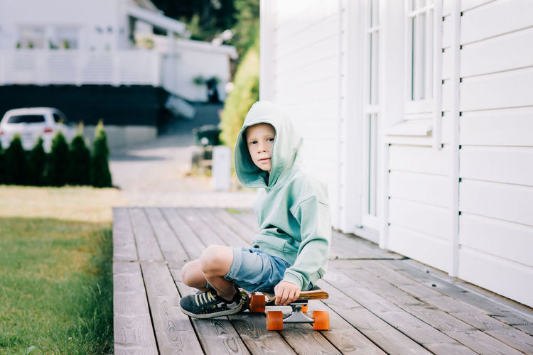 Young boy sat on a skateboard at home in a hoodie