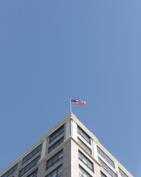 Low angle view of usa flag against building against clear blue sky