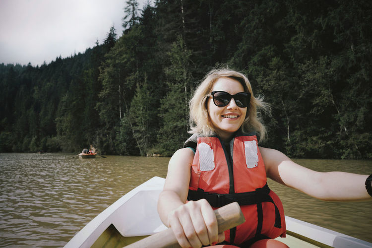 Smiling woman wearing sunglasses and life jacket sitting on boat in lake