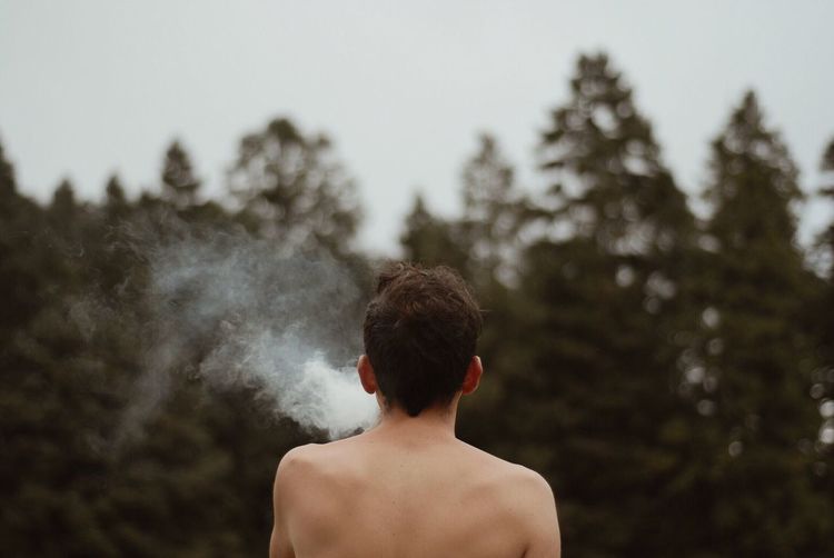 Rear view of man smoking against trees