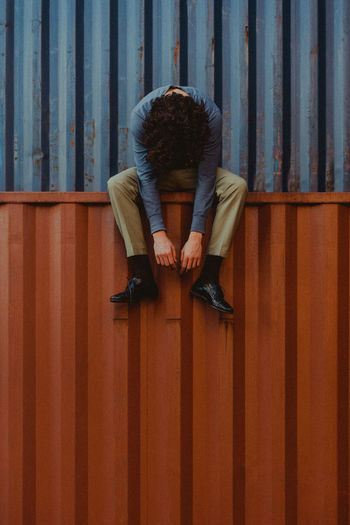 Full length of man sitting on wood against wall