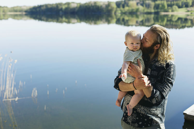 Man kissing baby son at lake