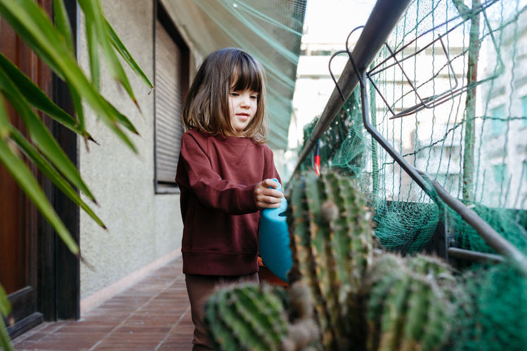 Child with brown hair watering plants at home balcony