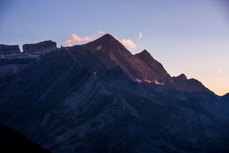 Peaks of picturesque mountain ridge located against sundown sky with clouds and moon in evening in pyrenees
