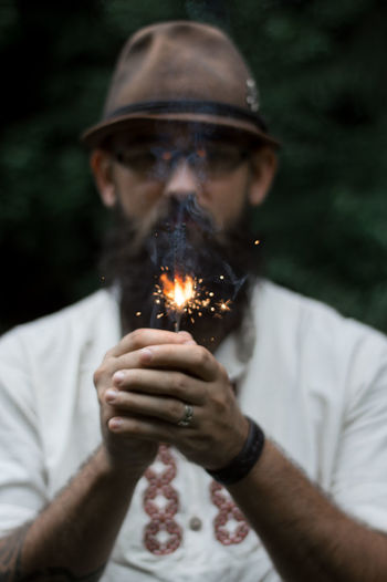 Portrait of young man burning sparkler while standing in forest