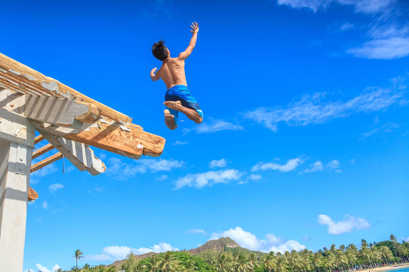 Low angle view of shirtless man jumping against blue sky