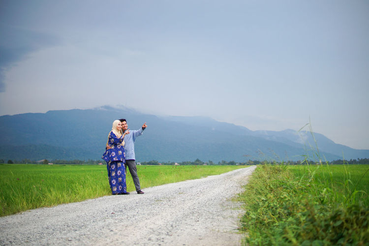 Woman standing on road amidst field against sky