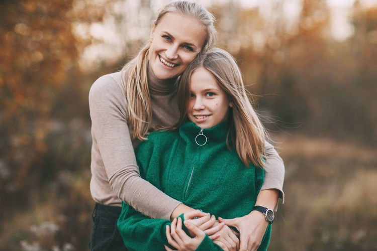 Portrait of happy mature mom and her blonde little daughter hugging and laughing while walking 