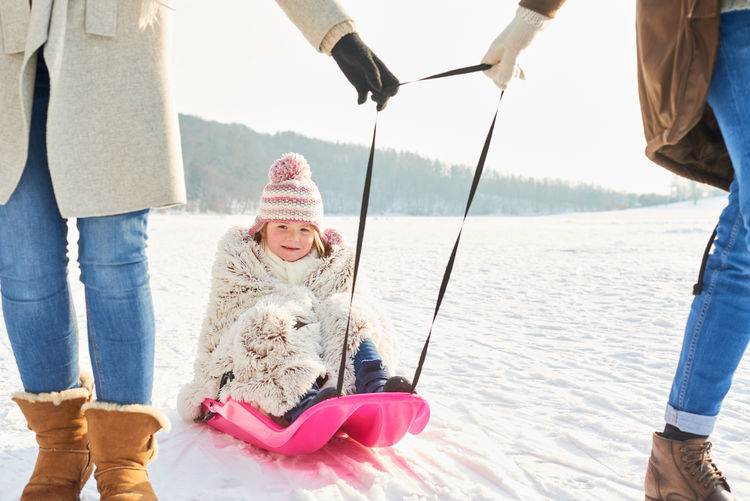 Low section of parents pulling girl sitting on sled