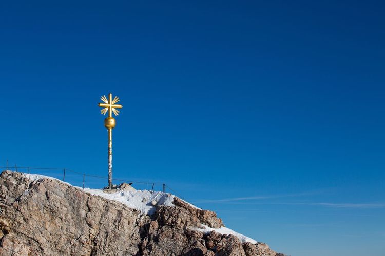 Low angle view of gold cross on mountain against clear blue sky on sunny day