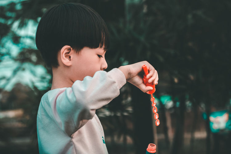 Close-up side view of boy blowing bubbles in park