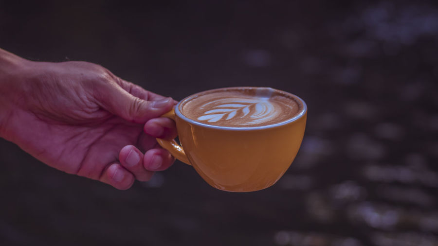 Hand holding a yellow cup of latte coffee top view showing latte art in leaf shape