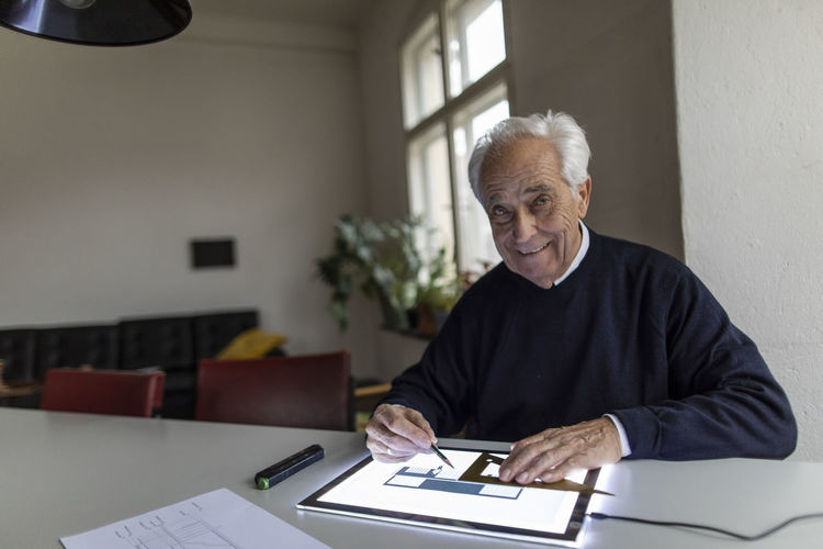 Portrait of smiling senior man using tablet with architectural plan